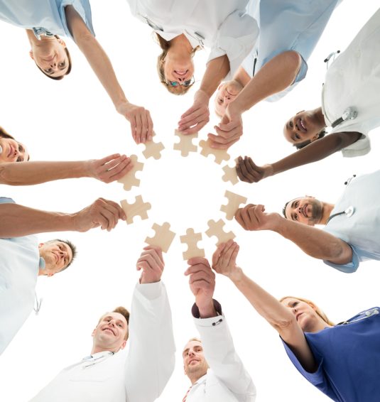 Directly below shot of medical team joining jigsaw pieces in huddle against white background